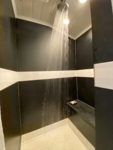 shower room with black walls and white horizontal stripe of tile half way up the wall. Water running form shower head