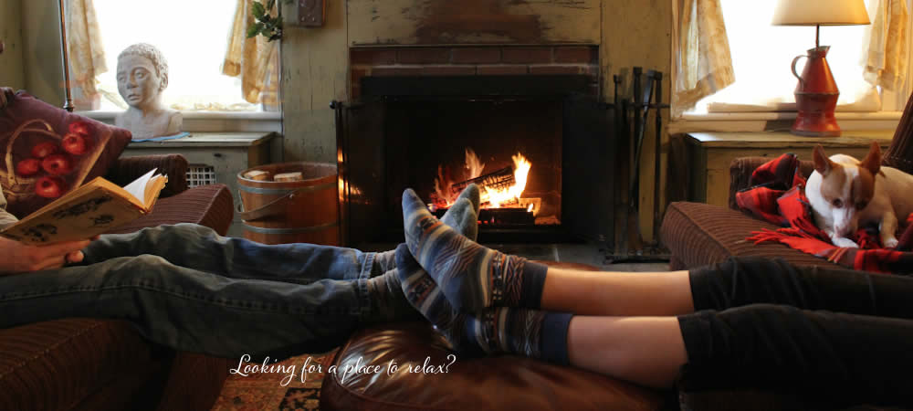 Two people sitting on opposite couches with their feet up on a mutual ottoman, in front of a roaring fireplace.