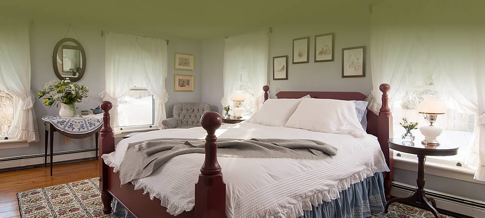 Four poster cherry bed with crisp white linens, a grey throw blanket and vintage pictures on the wall.