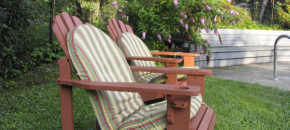 Two light brown adirondack chairs with striped seat pads sitting in a grassy area.